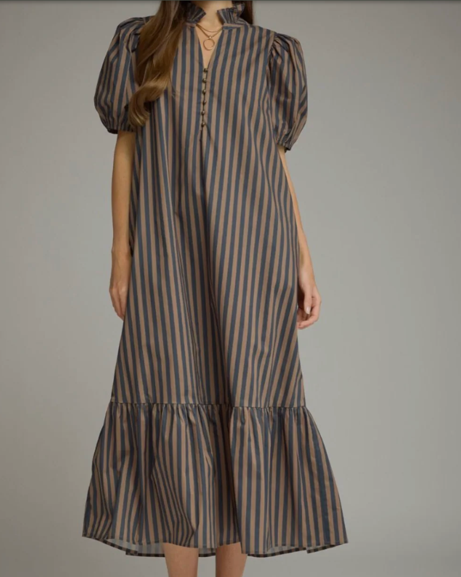 A woman wearing a midi-length puff-sleeve dress with vertical blue and beige stripes, a keyhole neckline with lace-up front, and a ruffled hem, photographed against a solid gray studio background.